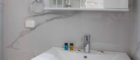 A bathroom with a white marble sink, a mirror above it, and a shower visible through the glass door.