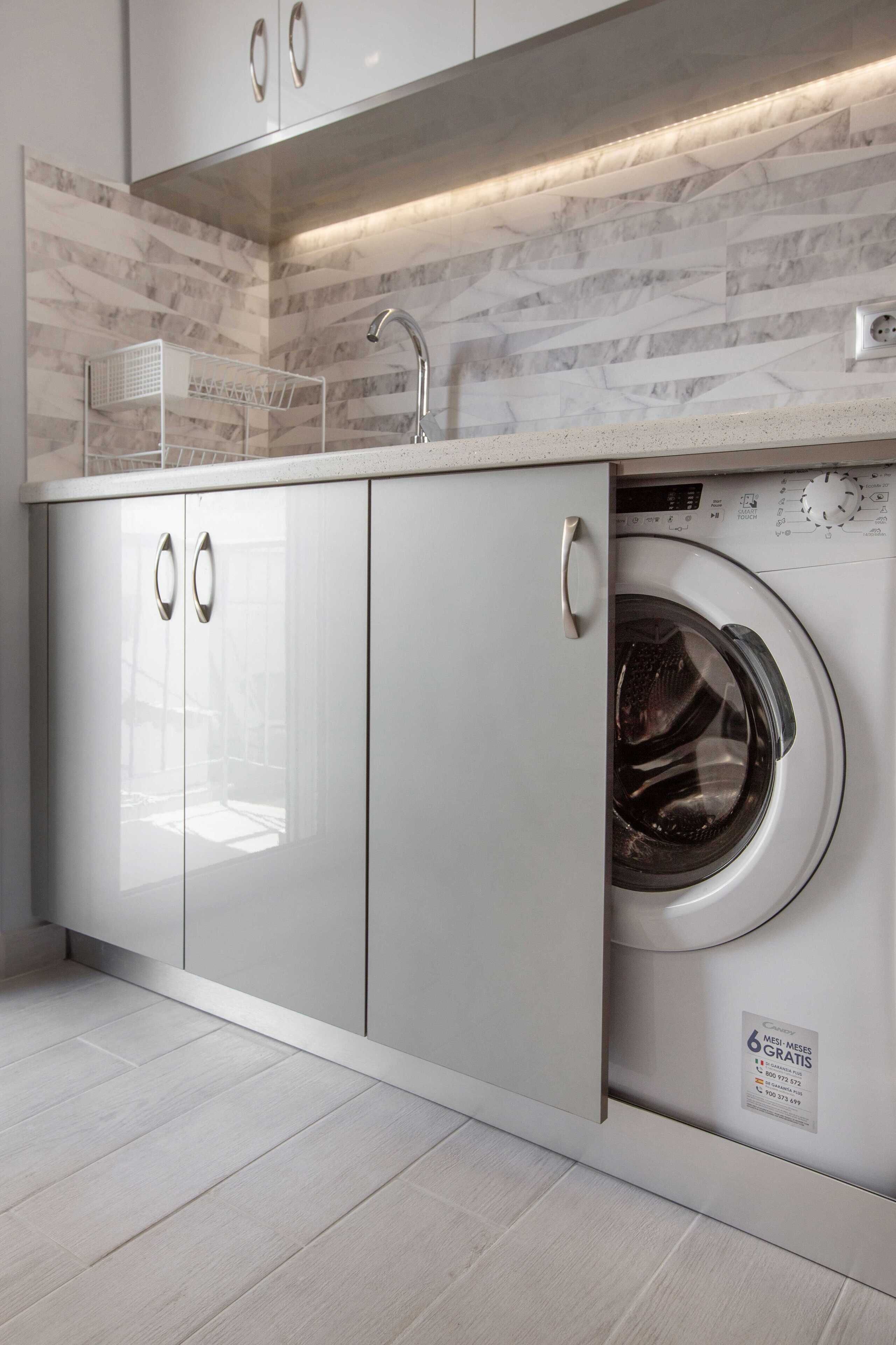 Une cuisine moderne dotée d’un lave-linge encastré, d’un évier en acier inoxydable et d’un dosseret en marbre.