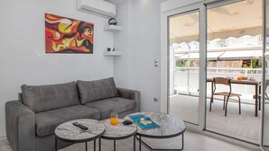 A modern living room with a grey sofa, two marble coffee tables, and a large window with a balcony view. - Studio penthouse near Acropolis by GHH (Athens)