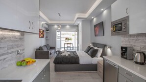 A compact, modern kitchen with integrated appliances, a dining area with a sofa and table, and a bedroom with a bed and bedside tables. - Studio penthouse near Acropolis by GHH (Athens)
