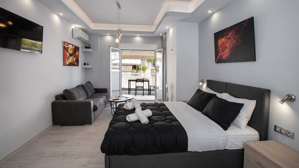 A modern bedroom with a large bed, a sofa, and a dining area visible through an open door. - Studio penthouse near Acropolis by GHH (Athens)
