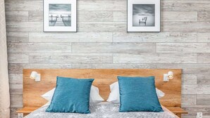 A bedroom with a wooden headboard, two blue pillows, a grey textured bedspread, and two framed pictures on the wall.