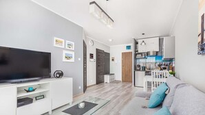 A modern living room with a flat-screen TV, a glass coffee table, and a grey sofa with blue cushions.