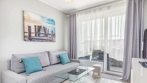 A modern living room with a grey sofa, a glass coffee table, and a painting of a pier.