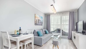 A modern living room with a grey sofa, white dining table, and a TV on a white cabinet.