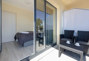 A modern bedroom with a bed, a sliding glass door leading to a balcony, and a seating area with a table and chairs.