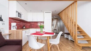 Una cocina moderna con armarios blancos, un salpicadero rojo y una escalera de madera.
