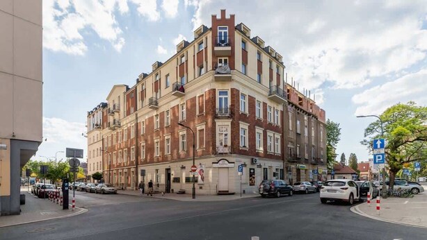 Un edificio de varios pisos con entrada en esquina, acceso visible al nivel de la calle y un letrero que indica zona de estacionamiento.