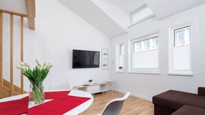 Una sala de estar moderna con un televisor de pantalla plana, un comedor con camino de mesa rojo y un sofá marrón.
