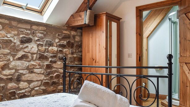 A bedroom with a stone wall, a wooden wardrobe, a bed with a floral bedspread, and a skylight. - 3 bedroom accommodation in Little Edstone, near Pickering (Little Edstone, near Pickering)
