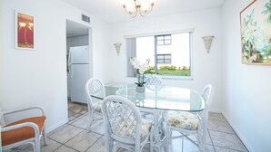 Un comedor con mesa de vidrio, sillas de mimbre y un refrigerador al fondo.