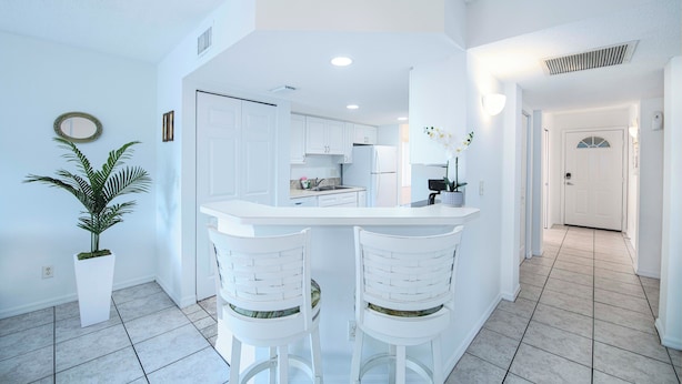 Una cocina moderna con gabinetes blancos, una isla central y dos taburetes de bar.