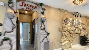 Un corridoio con un cartello 'Jurassic Park', un murale di dinosauri e un pavimento in legno.