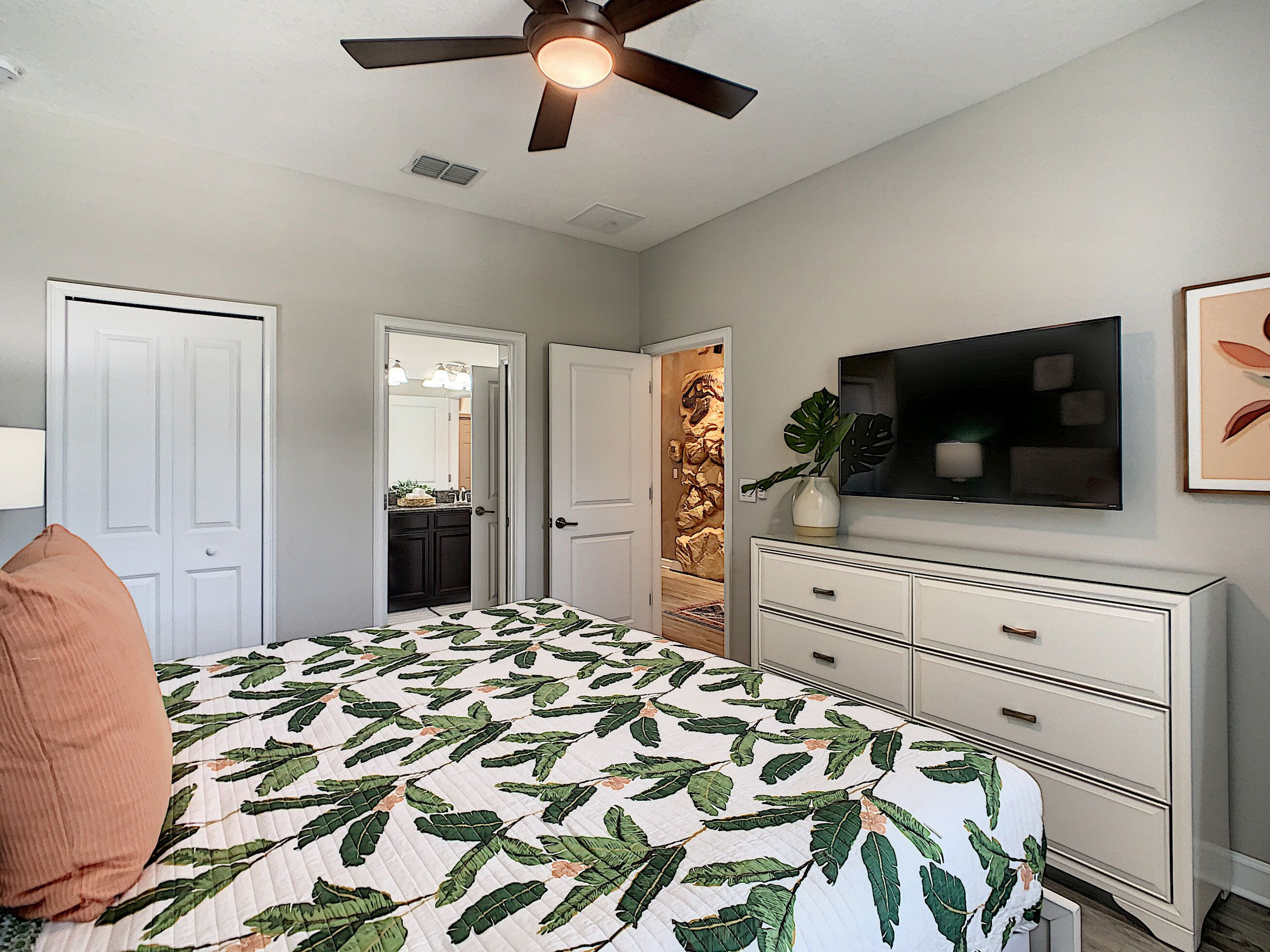 A bedroom with a bed, a dresser, a ceiling fan, a TV, and a door.