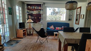 Un accogliente soggiorno con un divano blu, pavimento in legno, una libreria, una TV e un'area pranzo con tavolo e sedie.