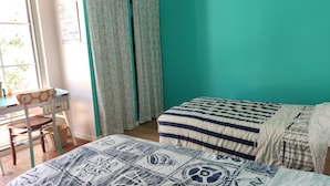 Una stanza con pareti color petrolio, una scrivania con sedia, due letti con coperte a fantasia e una finestra con tende.