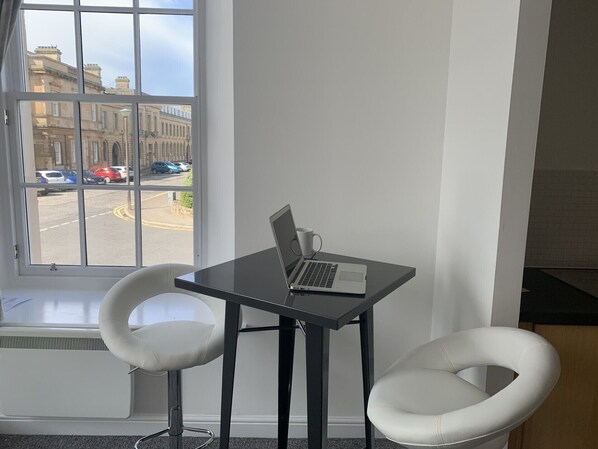 A room with a window view of a street, a table with a laptop, and two white chairs. - Ayr Cozy Corner Apartment (Ayr)
