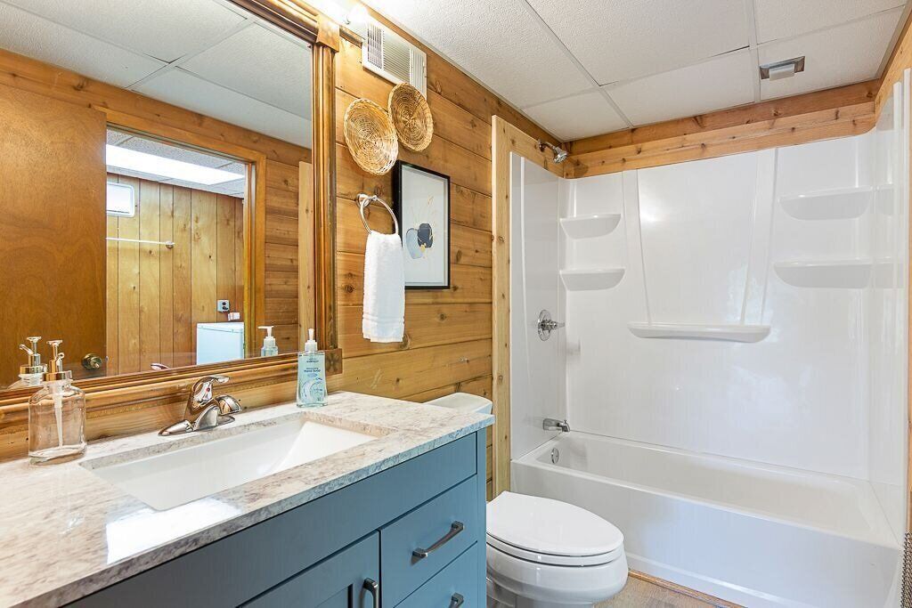 Een badkamer met houten lambrisering, een witte badkuip, een wastafel met een marmeren blad en een toilet.