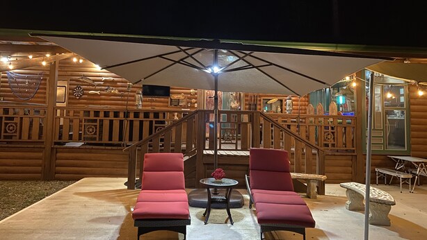 A log cabin with two red lounge chairs under a large umbrella, a wooden staircase, and a rustic interior with decorative items. - Poblado Log Cabin Camper  (Boquerón)