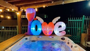 A hot tub with inflatable decorations spelling "LOVE" and a wooden deck with string lights. - Poblado Log Cabin Camper  (Boquerón)