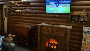 A cozy room with a wooden log wall, a television mounted above a fireplace, and various decorative items like fish and a dartboard. - Poblado Log Cabin Camper  (Boquerón)