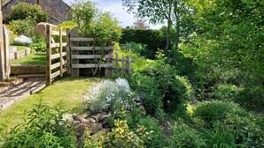 A rustic stone building with a wooden gate, surrounded by lush greenery and a well-maintained garden. - Gorgeous Stone Cottage with tasteful interior (Chathill)