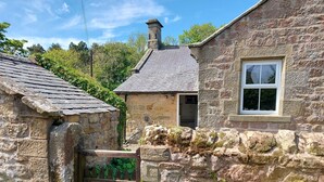 A stone cottage with a wooden gate, a small window, and lush greenery. - Gorgeous Stone Cottage with tasteful interior (Chathill)