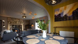 A cozy living room with a stone fireplace, a round dining table with placemats, and a large painting on the wall. - Gorgeous Stone Cottage with tasteful interior (Chathill)