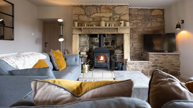 A cozy living room with a stone fireplace, a sofa, and a television. - Gorgeous Stone Cottage with tasteful interior (Chathill)
