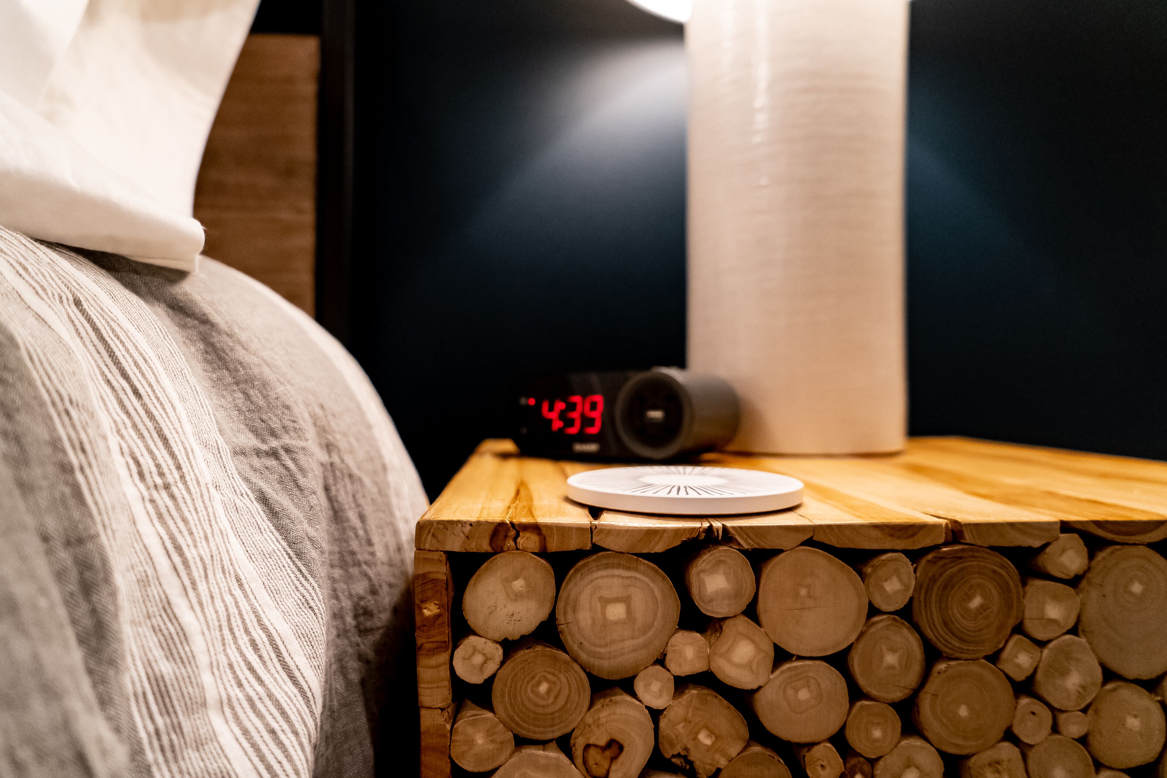 A wooden nightstand with a clock displaying 4:39, a white plate, and a roll of paper towels.