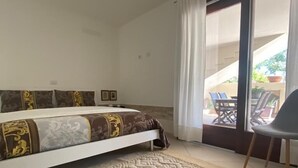 A bedroom with a bed, a green ottoman, a patterned rug, and a sliding glass door leading to an outdoor area with chairs. - Villa Luigi in Poggio dei Pini: villa accommodation with parking and wallbox (Capoterra)
