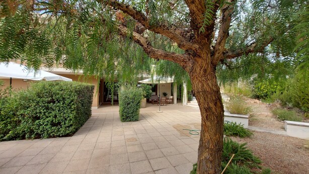 A courtyard with a paved walkway, a dining area with outdoor furniture, and a large tree providing shade. - Villa Luigi in Poggio dei Pini: villa accommodation with parking and wallbox (Capoterra)