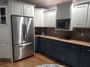 A kitchen with white cabinets, a stainless steel refrigerator, a microwave, and a coffee maker.
