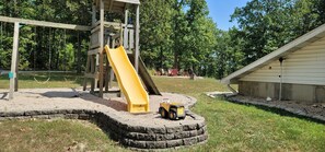 A playground with a yellow slide, a wooden play structure, and a toy dump truck.