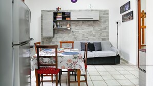 Un espacio habitable compacto con una mesa de comedor, sillas, un sofá, una estantería empotrada y un refrigerador.
