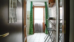 Un pasillo con suelo de baldosas, una puerta con manija, una silla y una estantería con objetos.
