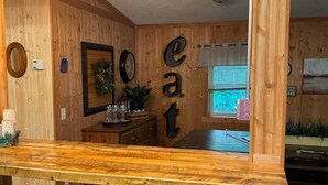 A wooden interior with a bar area, stools, and a fireplace. - Whispering Pines Lakeside Retreat  (Park Rapids)