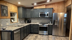 A modern kitchen with dark cabinets, a stainless steel refrigerator, a microwave, and a stove. - Whispering Pines Lakeside Retreat  (Park Rapids)