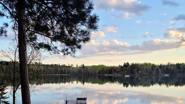 A lakeside campfire with a dock and a wooden structure in the background. - Whispering Pines Lakeside Retreat  (Park Rapids)