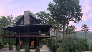 Ein großes Holzhaus mit einem Steinsschornstein, einem Balkon und einer Veranda mit Sitzgelegenheiten.