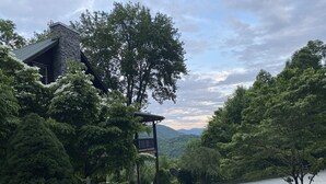 Eine Holzhütte mit Steinverkleidung, umgeben von dichtem Wald und freiem Blick auf ferne Berge.