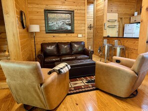 Ein Holzhütten-Interieur mit einer Ledersofa, zwei Sesseln, einem Essbereich mit Tisch und Stühlen sowie einer Küche mit Geräten.
