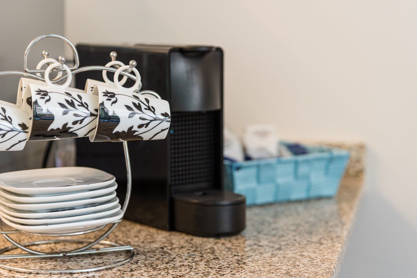 Uma bancada de cozinha com uma pilha de pratos brancos, uma máquina de café e uma caixa de armazenamento azul.