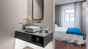 A modern bathroom with a large mirror, a white sink, and a small vase with flowers.