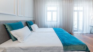 A hotel room with two beds, a large window with sheer curtains, and a view of the outdoors.