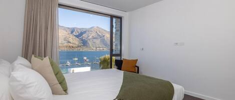 A bedroom with a large bed, a view of a lake and mountains, and a window with curtains.