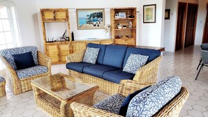 A living room with a blue sofa, two wicker armchairs, a coffee table, and a wooden cabinet with shelves. - Private Waterfront  Home With 180* Sea Views - 2 Bed / 2Bath (Spanish Wells)