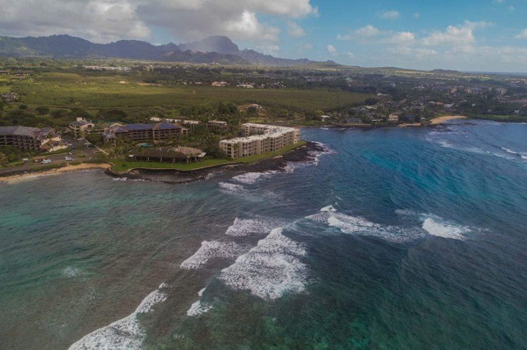 A coastal resort with multiple buildings, a beachfront, and a view of distant mountains.
