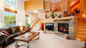 A spacious living room with a fireplace, a leather sofa, a coffee table, and a staircase leading to a kitchen area. - Luxury Downtown Condo - Private Hot Tub! Walk to Dining and Ski Bus... (Winter Park)