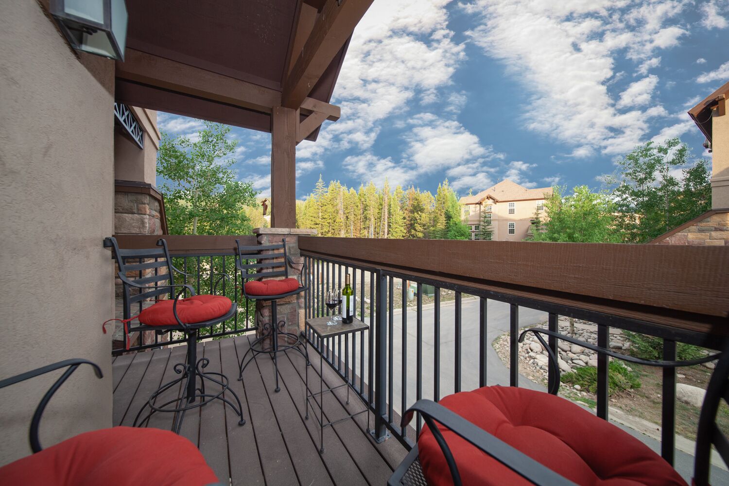 A wooden deck with outdoor seating, a stone pillar, and a view of trees and buildings.